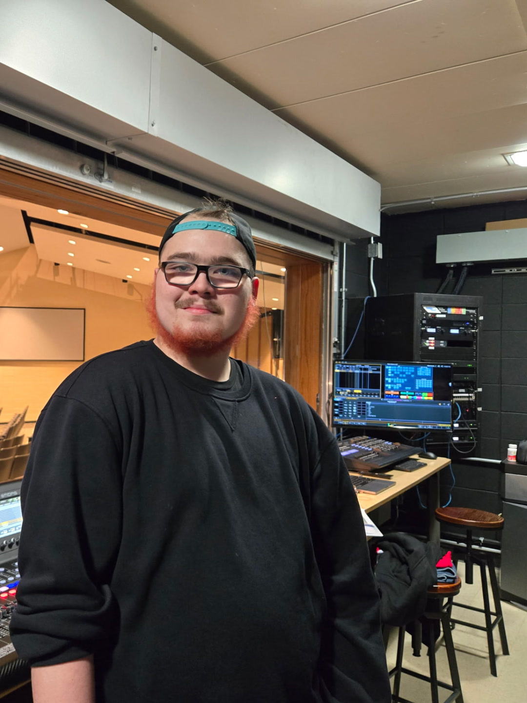 Mason Hintz standing at a live sound mixing console in a theater control booth